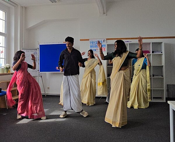 Indische Schülerinnen und ein indischer Schüler tanzen ausgelassen im Klassenzimmer – alle in traditionellen Outfits, mit sichtbarer Freude in ihren Gesichtern.