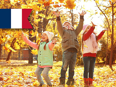 Drei fröhliche Kinder spielen im Herbstlaub. Gelbe Blätter bedecken den Boden. Französische Flagge oben links. 