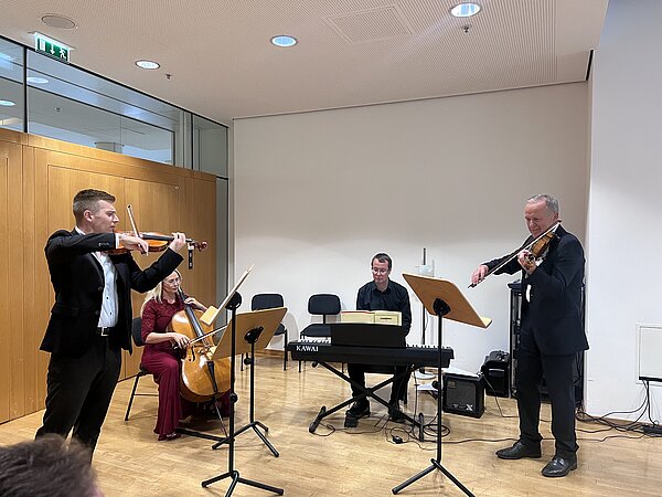 Ein vierköpfiges Ensemble mit zwei Geigen, Violoncello und Keyboard spielt bei einer Veranstaltung vor Publikum.