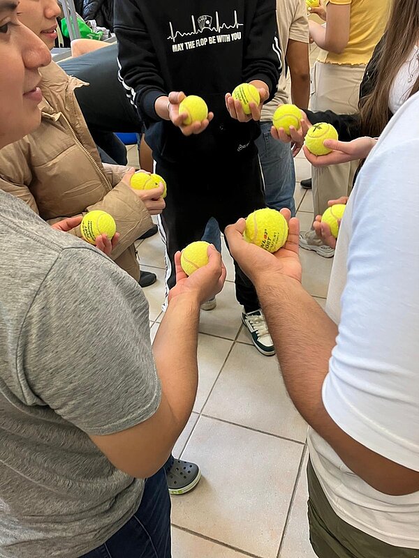 Auszubildende stehen beieinnander, halten alle Tennisbälle in den Händen und strecken die Arme in die Mitte zueinander. 
