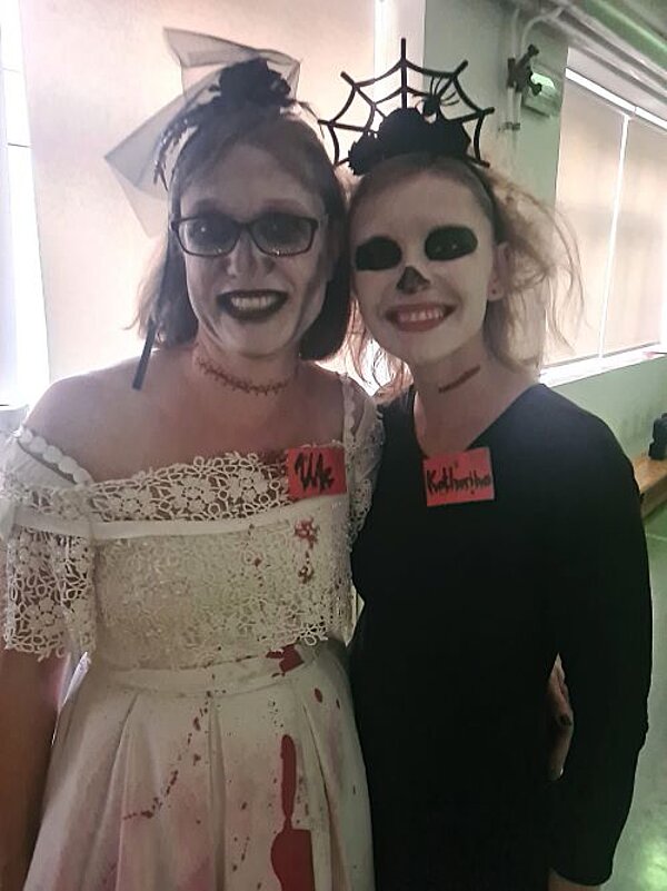 Zwei Personen in Halloweenkostümen mit stark geschminkten Gesichtern stehen nahe beieinander und lächeln. 