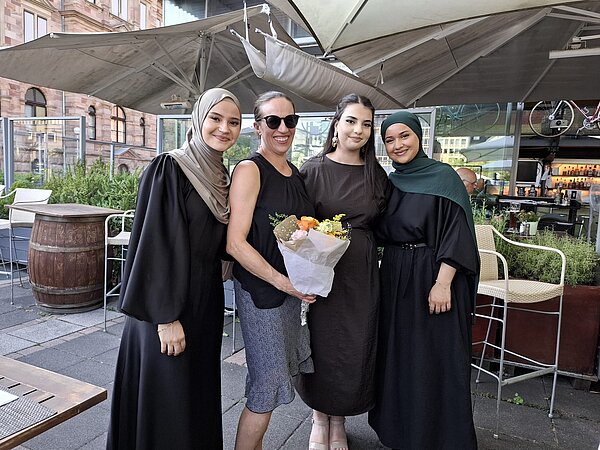 Gruppenfoto von vier Personen auf einer Restaurantterrasse, eine Person hält einen Blumenstrauß vor sich.