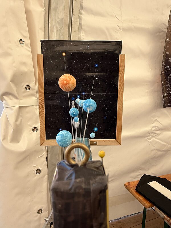 Räumliches Modell des Sonnensystems mit farbigen Planetenkugeln vor einem Sternenhintergrund in einem Holzrahmen.