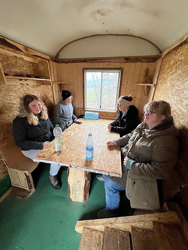 Vier Schüler*innen sitzen in einem Bauwagen an einem Tisch.