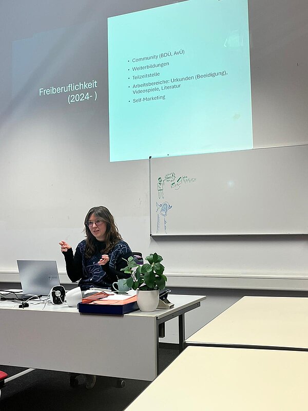 Eine Referentin spricht in einem Seminarraum über Freiberuflichkeit und berufliche Perspektiven, während eine Präsentationsfolie an die Wand projiziert wird.