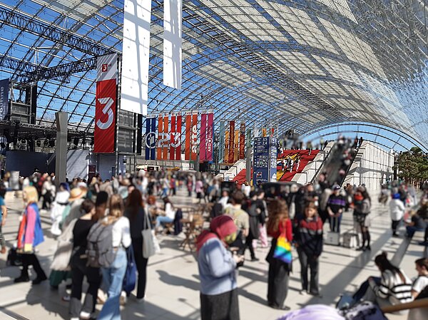 Buchmesse Leipzig: Wo Worte Bildung und Austausch fördern Szene in der sonnigen Messehalle mit gläsernen Kuppel. Die Menschen, die sich dort tummeln, sind nur verschwommen zu erkennen.
