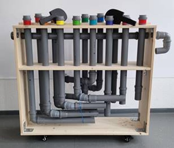 Instrumentenbau an der Euro Akademie Riesa Schülerinnen und Schüler der Euro Akademie Riesa bauen ein sogenannten Tubulum-Röhreninstrument, das aus 14 grauen Röhren uns Plastik besteht, die in einen Holzrahmen gefasst sind.