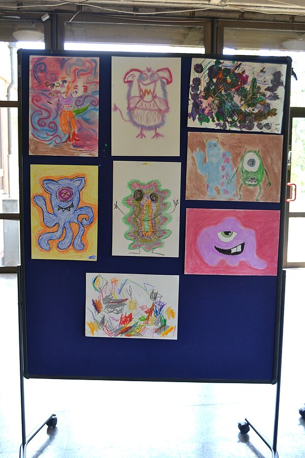 Vernissage in der Christopherus-Schule Eine Stellwand mit bunt bemalten Bildern steht in einem hellen Raum mit großen Fenstern.