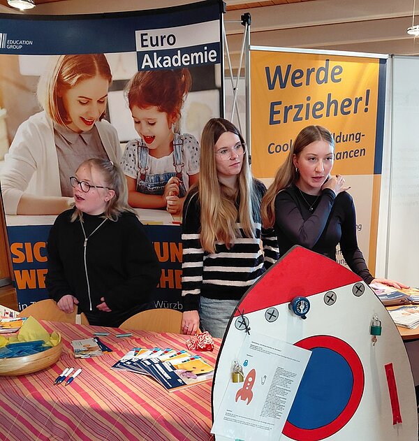 Karriere mit Herz Drei weibliche Auszubildende stehen am Messestand der Euro Akademie und beraten Interessierte zu ihren Ausbildungen.