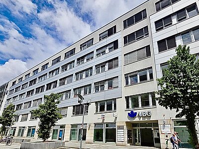 Gebäude der Euro Akademie Dresden, mit Ladenzeile unten und Baum.