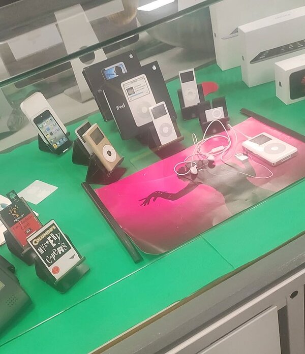 Ausstellung historischer Apple-Produkte wie iPods, iPhones und Zubehör in einer Vitrine.