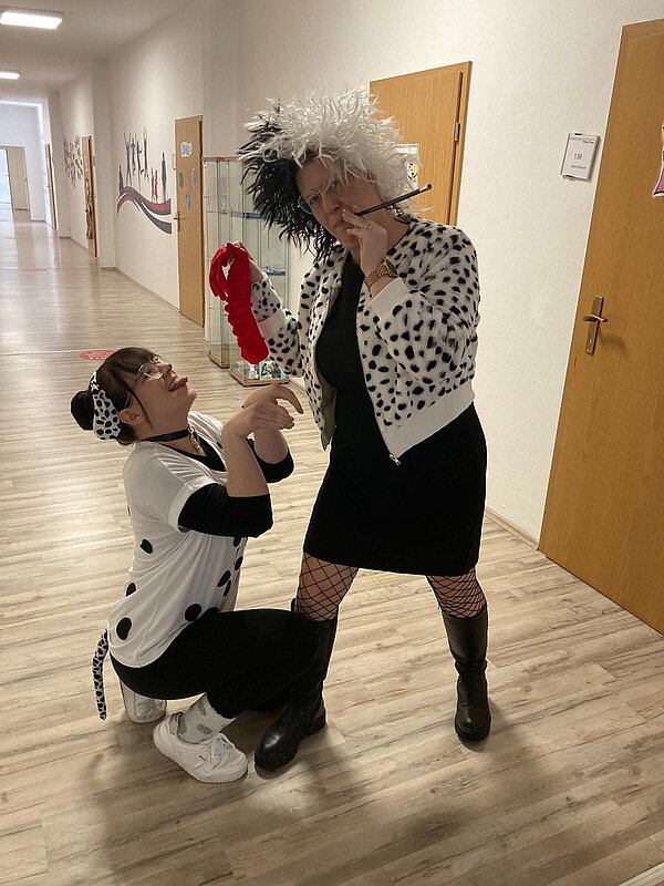 Helau und Alaaf in Rochlitz Zwei Frauen in Kostümen stehen in einem Flur. Eine ist als Dalmatiner verkleidet und hockt verspielt auf dem Boden, während die andere als Cruella de Vil in einem schwarz-weißen Outfit mit Perücke, Zigarettenspitze und rotem Handschuh posiert.