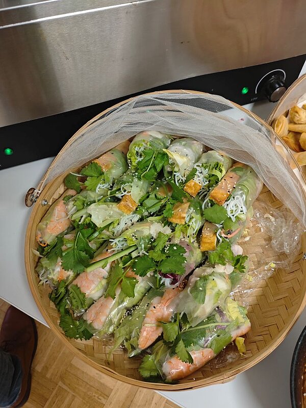 Eine große Schüssel gefüllt mit vietnamesischen Frühlingsrollen, die mit Garnelen, Kräutern, Reisnudeln und Gemüse gefüllt sind. Die Rollen sind mit transparentem Reispapier umwickelt und mit frischem Koriander garniert.