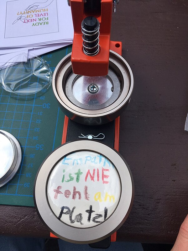 Protesttag zur Gleichstellung von Menschen mit Behinderung: Buttons für Inklusion Ein neuer Button wird gerade in die Maschine eingespannt. Auf ihm steht mit bunten Stiften geschrieben: Empathie ist NIE fehlt am Platz!