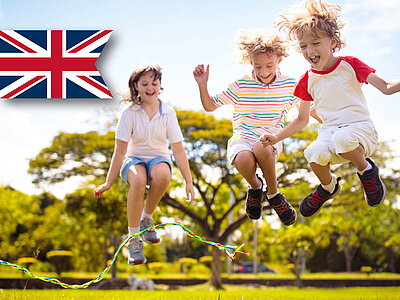 Drei Personen springen Seil unter sonnigem Himmel, britische Flagge im Hintergrund.