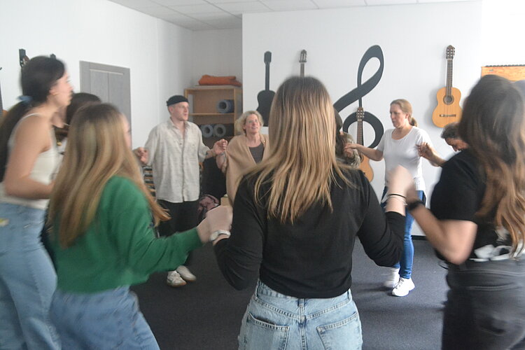Mädchen und junge Frauen tanzen in einem großen weißen Raum, an dessen Wände Noten in Schwarz angemalt sind.