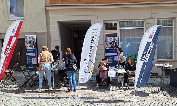 Menschen informieren sich am Stand der Euro Akademie und der Euro-Schulen Hohenstein-Ernstthal beim Frühlingsfest „HOT im Herzen“. Aufsteller und Banner zeigen das Bildungsangebot, während Kinder und Erwachsene an Tischen basteln.