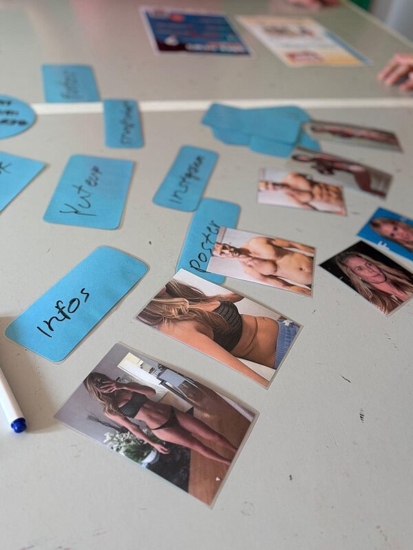 Auf einem Tisch liegen freizügige Fotos von jungen Menschen zum Stichwort Sharing. Stichworte dazu liegen auf kleinen blauen Notizzetteln darüber.