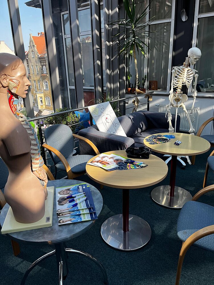 Drei runde Tische stehen in der Mitte von mehreren Stühlen. Auf zwei der Tische stehen Oberteile von Skeletten.