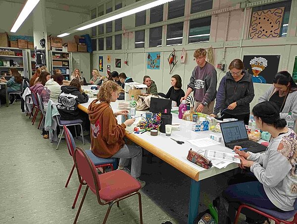 Schülerinnen und Schüler sitzen an einem langen Tisch mit Müll und recyceln diesen zu neuen Objekten. 