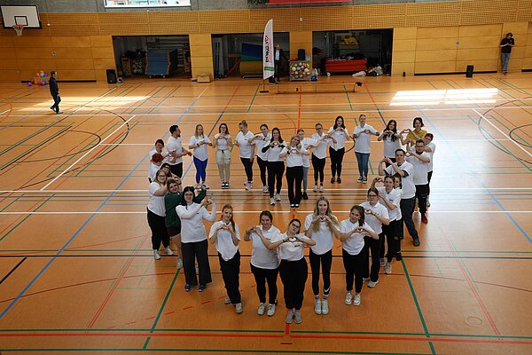 Auszubildende der Euro Akademie Pößneck unterstützen erneut den „Pokal des Bürgermeisters“ Die Schülerinnen und Schüler formieren mitten auf dem Parkett der Turnhalle ein Herz, das von einer erhöhten Position fotografiert wurde.