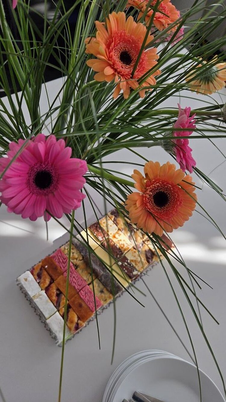 Ein Blumenstrauß mit pinken und orangenen Gerbera, daneben eine Schachtel Pralinen.