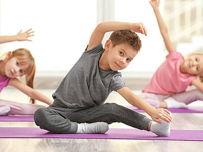 Das Bild zeigt Kinder, die Yoga praktizieren. Es betont die Bedeutung von körperlicher Aktivität und Wohlbefinden bereits im jungen Alter.