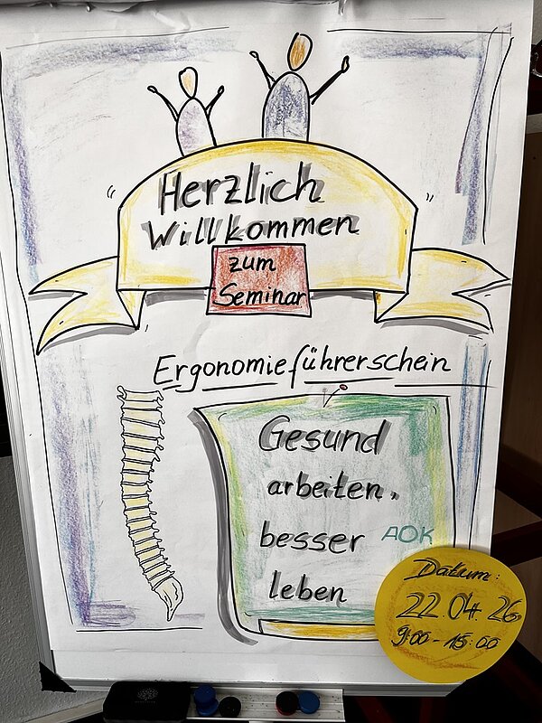 Handgezeichnetes Plakat mit mehreren farbigen Elementen. Oben sind zwei stilisierte Figuren mit erhobenen Armen zu sehen, darunter ein gelbes Banner mit der Aufschrift 'Herzlich Willkommen zum Seminar'. In der Mitte steht 'Ergonomieführerschein'. Links daneben ist eine stilisierte Wirbelsäule gezeichnet. Im unteren Bereich befindet sich ein grünes Feld mit dem Text 'Gesund arbeiten, besser leben' und dem Logo der AOK. Unten rechts ist ein gelber Kreis mit dem handschriftlichen Text 'Datum: 22.04.26 9:00 - 15:00'.