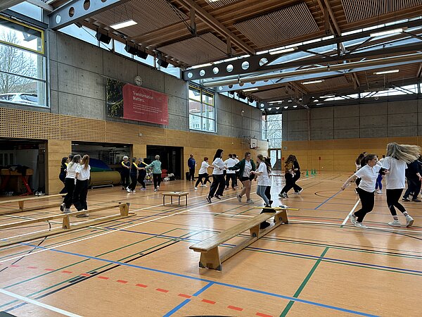 Auszubildende der Euro Akademie Pößneck unterstützen erneut den „Pokal des Bürgermeisters“ Szene in einer Turnhalle: Mehrere Menschen tanzen paarweise miteinander. Dazwischen stehen Holzbänke. Die Garagentore der Materialräume stehen offen.