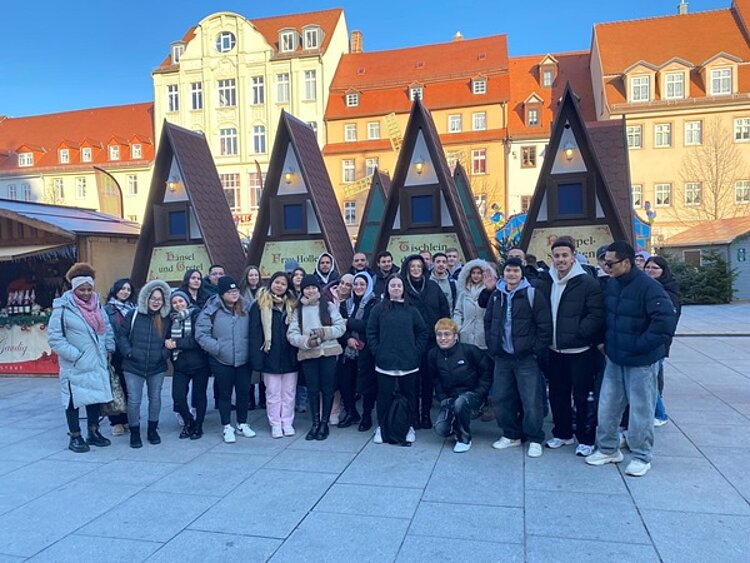 Schüler stehen vor Verkaufsbuden auf dem Weihnachtsmarkt in Weißenfels und posieren für ein Gruppenfoto.
