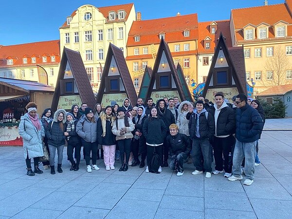 Schüler stehen vor Verkaufsbuden auf dem Weihnachtsmarkt in Weißenfels und posieren für ein Gruppenfoto.