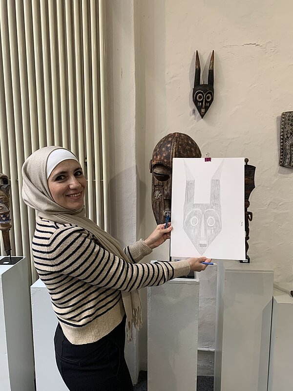 Im Bann der Masken Schülerin zeigt ihr gezeichnetes Bild eines altes afrikanischen Maskenexponates in die Kamera.