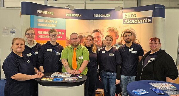 Gruppenbild von acht Euro Akademie-Mitarbeitern und Mitarbeiterinnen an ihrem Messestand.