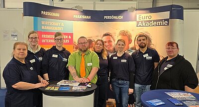 Gruppenbild von acht Euro Akademie-Mitarbeitern und Mitarbeiterinnen an ihrem Messestand.