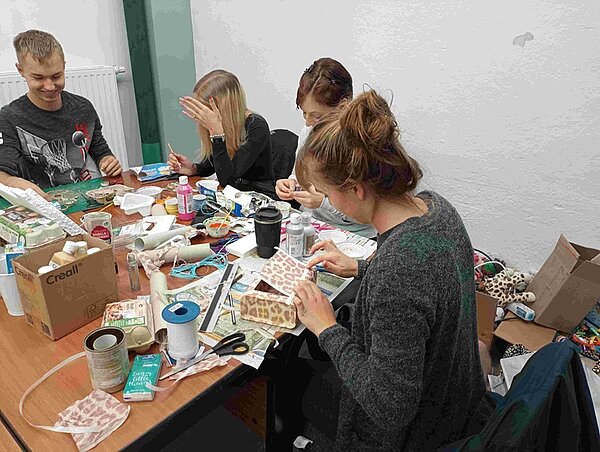 Schülerinnen und Schüler sitzen an einem Tisch und recyceln Müll zu neuen Objekten. 