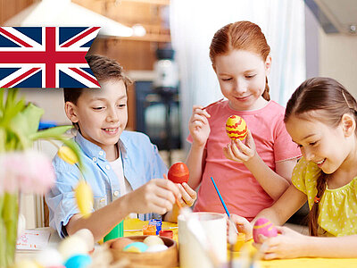 Das Bild zeigt Kinder, die Ostereier bemalen und im Hintergrund ist eine britische Flagge zu sehen.