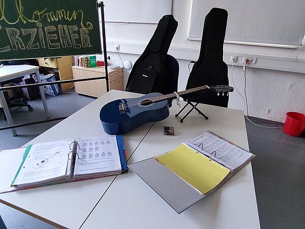 Erfolgreicher Tag der offenen Tür Auf einem Tisch im Klassenraum liegt eine Akustikgitarre und zwei Ringordner mit Noten und Lieder.