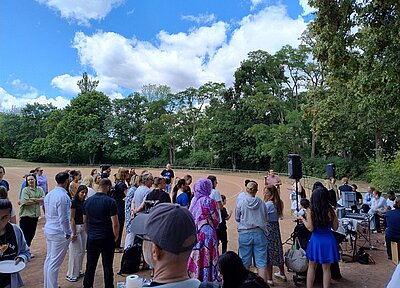 Schnappschuss in die Menge der Schülerinnen, Schüler und Lehrkräfte der Euro Akademie, die sämtlich bei sommerlichem Wetter draußen das Sommerfest gemeinsam genießen.