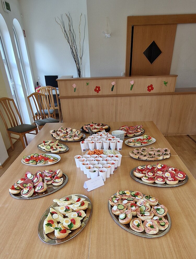 Berufspädagogische Pflichtfortbildung an der Euro Akademie Pößneck Belegete Weißbrotbrötchen liegen auf einem silbernen Tablett und sind belegt mit Käse, Tomate, Gurke und verschiedener Wurst. Dort herum stehen gestapelte Becher.