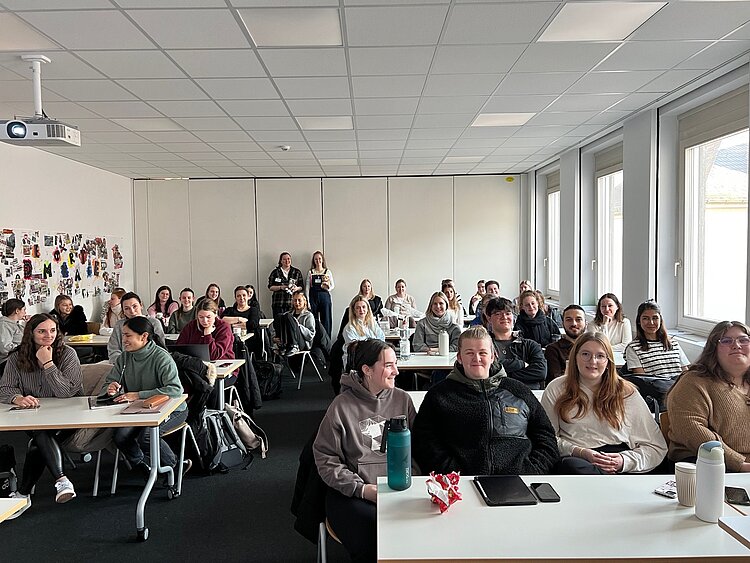 Wo die Katze nicht gestreichelt werden will Ein Klassenzimmer ist prall gefüllt mit Schülerinnen (in erster Linie) und Schülern, zwei von ihnen stehen sogar ganz hinten an der Wand. Die Personen scheinen allesamt sehr fröhlich zu sein.