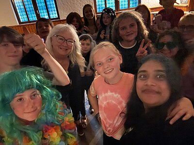 Eine fröhliche Gruppe von Leuten macht ein Selfie, links unten eine Frau mit auffälliger Perücke.