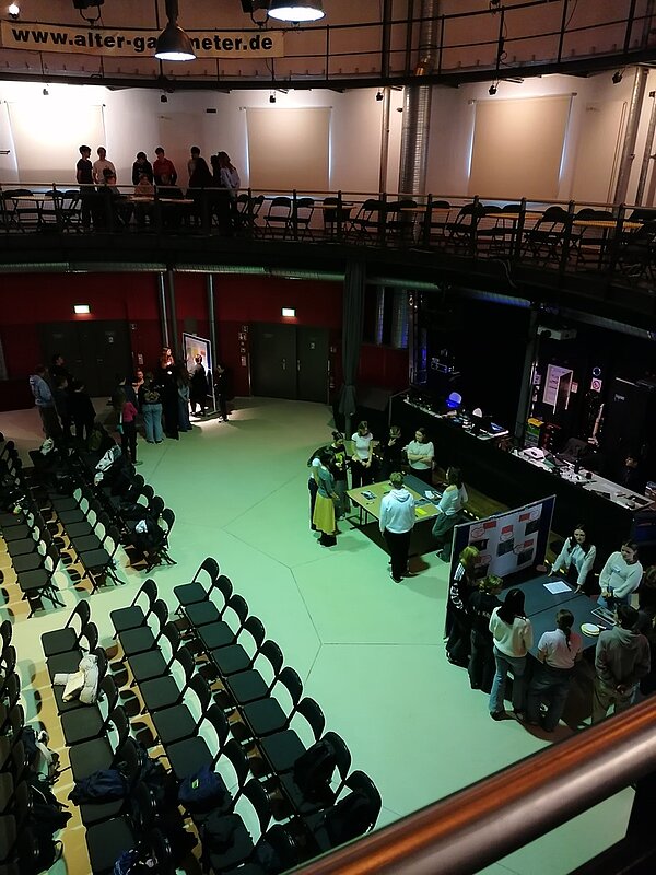 Blick aus der Vogelperspektive in den großen Saal des Alten Gasometers. Es sind viele Stuhlreihen zu sehen und aufgebaute Tische, an denen die Schülerinnen und Schüler in Gruppenarbeit das Thema erörtern.