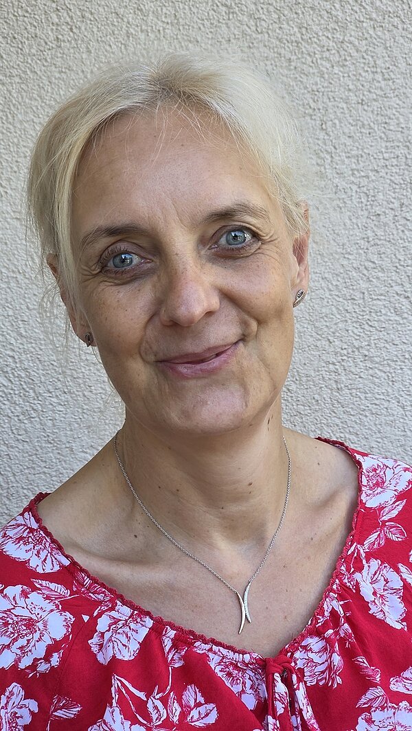 30 Jahre Ausbildung im Fachbereich Physiotherapie Porträtfoto der Mitarbeiterin Ilka Hofmann, die in einer rot-weißen Bluse, mit einer goldenen Kette um den hals freundlich in die Kamera lächelt.