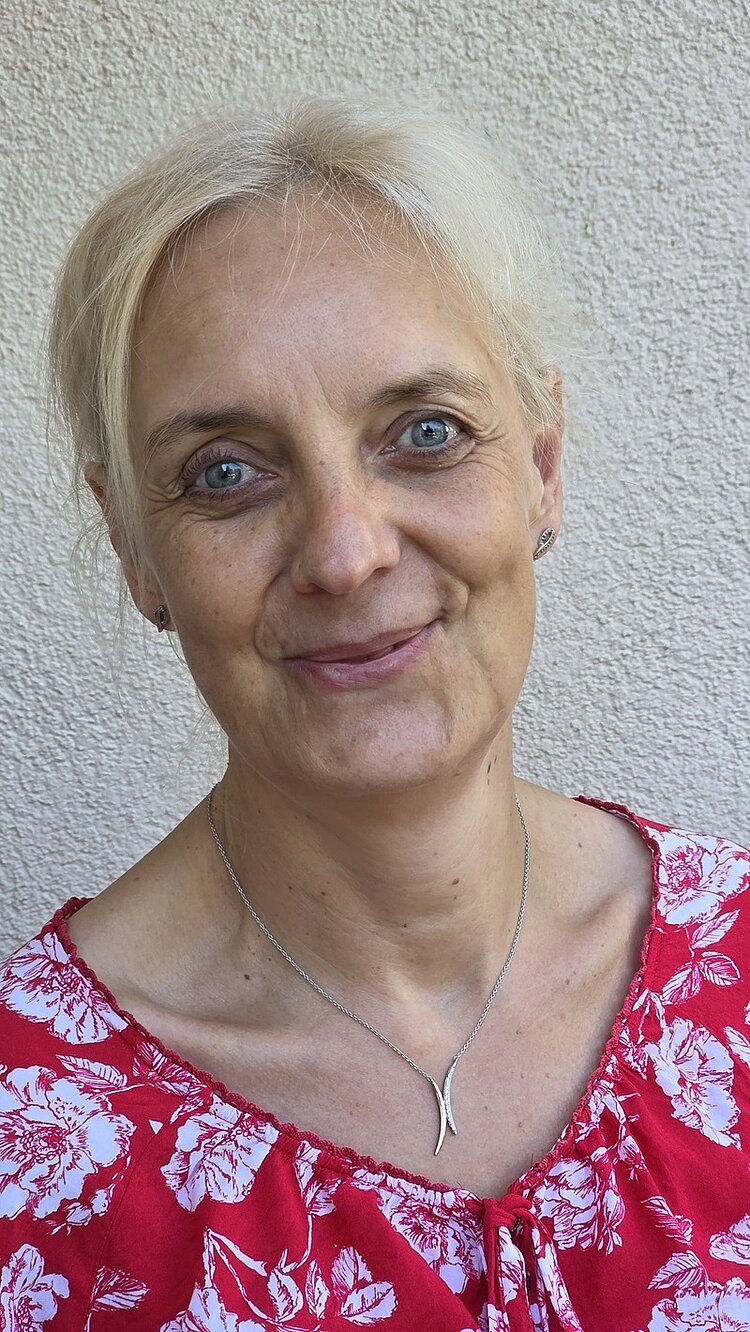 30 Jahre Ausbildung im Fachbereich Physiotherapie Porträtfoto der Mitarbeiterin Ilka Hofmann, die in einer rot-weißen Bluse, mit einer goldenen Kette um den hals freundlich in die Kamera lächelt.