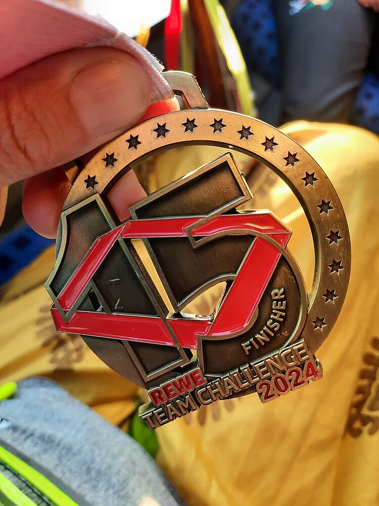 REWE Team Challenge 2024 Nahaufnahme einer Medaille mit der Aufschrift "Finisher REWE Team Challenge 2024" und einer 15 in große Zahlen.