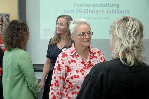 Mehrere Frauen unterhalten sich bei der Festveranstaltung zum 35-jährigen Jubiläum der Euro Akademie. Im Hintergrund ist eine Präsentationsfolie mit dem Schriftzug „Festveranstaltung zum 35-jährigen Jubiläum“ zu sehen.
