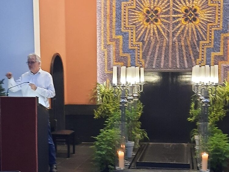 Unterricht einmal anders – Ethik trifft medizinische Fachsprache Der Leiter des Krematoriums steht an einem Podest, links neben im stehen auf dem Boden Trauerkerzen, und viele Kerzenständer mit weißen Kerzen. Im Hintergrund ein großes Mosaik an der Wand.