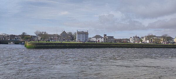 Panoramablick auf eine Stadt am Flussufer mit historischen Gebäuden und einer Promenade.