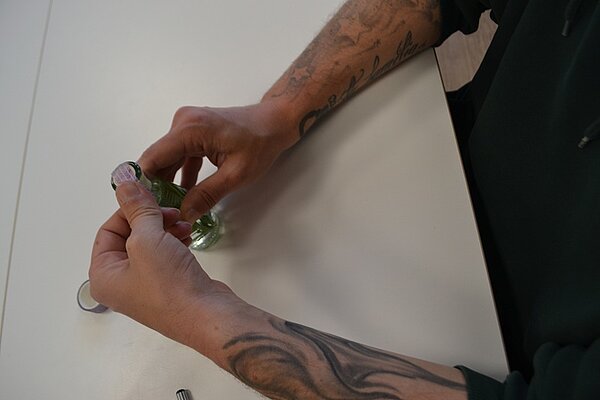 Zwei tättowierte Arme, die eine kleine 0,33 l Flasche zukleben. 