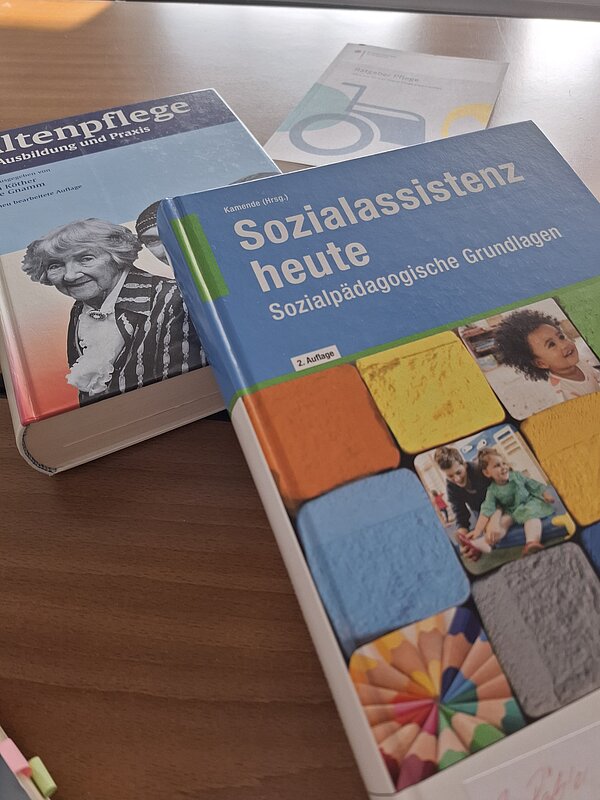 Fachbücher zu Sozialassistenz, Altenpflege und Patientenpflege liegen auf einem Tisch und verweisen auf Ausbildungsinhalte im sozialen und pflegerischen Bereich.